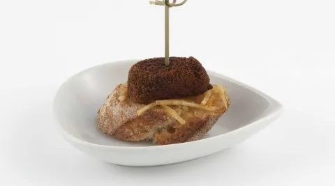 Croqueta de asado sobre cama de patatas paja y cebolla caramel·litzada