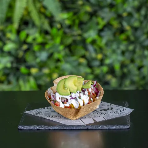 Torta de maíz horneada simulando un nido donde reposa arroz basmati, tinga de pollo, pico de gallo y aguacate con un toque de salsa de yogur