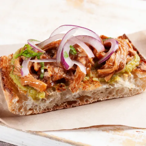 Panecillo tostado con pulled pork, guacamole, cebolla morada y cilantro.