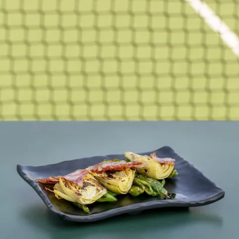 Alcachofas a la brasa con salsa de pipas tostadas y crujiente de jamón ibérico de cebo 50 % , con una base de pimientos