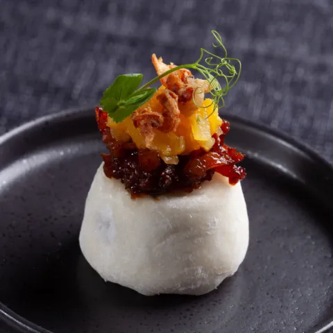 Mochi relleno de mousse de queso azul y nueces, con mermelada de beicon y teriyaki, frutas caramelizadas y un toque de cebolla crujiente.