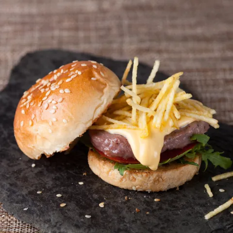 Hamburguesa mixta con tomate, rúcula, salsa cheddar, sésamo y patatas paja.