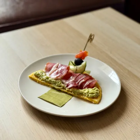 Base de arepa de maíz amarillo colombiana, guacamole, jamón ibérico, tomate, pepino y aceituna negra