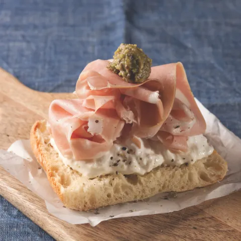 Pan de coca crujiente coronado con una suave stracciatella italiana, delicada mortadela y un toque de crema de pistacho