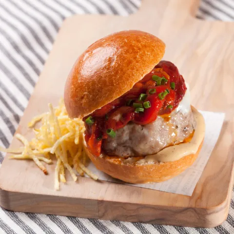 Pan de brioche, hamburguesa, mayonesa de ajo, pimiento asado y patatas paja.