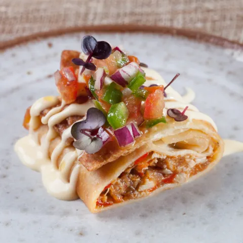 Burrito mexicano frito y crujiente, relleno de pollo salteado con cebolla y pimientos, bañado con salsa cremosa de cheddar y rematado con pico de gallo.