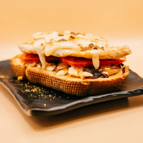 Base de pan moreno con pollo, cebolla frita, tomate, queso curado y salsa africana.