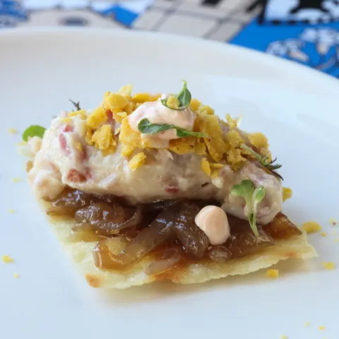 Crujiente de pan carasatu, relleno cremoso de croqueta de jamón ibérico ligado con salsa soubise, cebolla caramelizada, toque de mayonesa kimchi, polvo de totopo y micromezclum