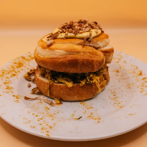 Pan brioche con pollo braseado marinado con salsa africana, mayonesa de curry y miel con cebolla crujiente. 