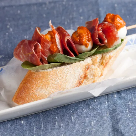 Perlas de mozzarella con jamón ibérico y pesto rojo sobre una tostada aromatizada con aceite de oliva y brotes tiernos.