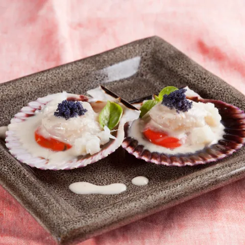 Vieira a la plancha, acompañada de finas virutas de bacalao desmigado, bañada con una suave crema del tradicional ajoblanco y coronada con perlas de arenque que simulan un falso caviar.