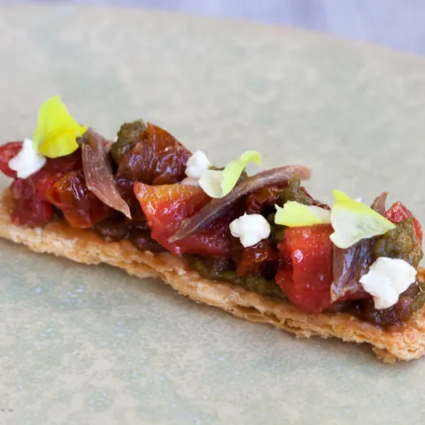 Coca con tomate asado, crema de queso ahumado, anchoa, pesto, pistachos y albahaca