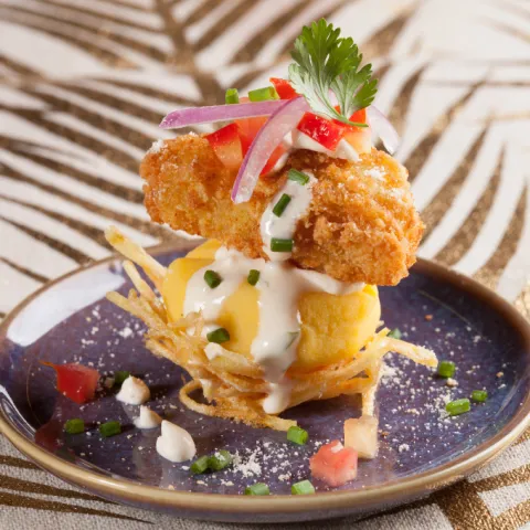 Base de causa coronada amb un niu cruixent de patata, xixarró de peix i mantega de llet de tigre. Es completa amb una emulsió de maionesa acevichada, ceba vermella i una fina terra de blat de moro chulpe torrat i ají limo deshidratat.