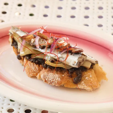 Tostada con tapenade, sardinillas picantes, alcachofas confitadas, miel, almendra tostada e hilos de chile