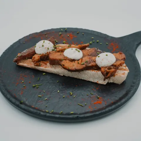 Zona A. Un viaje de ida entre el fuego y el sabor. Secreto marinado con mostaza antigua, soja, miel y especias, cocinado lentamente hasta alcanzar su punto perfecto y rematado con una suave mayonesa de trufa. Una tapa que suena a verano desde el primer bocado.