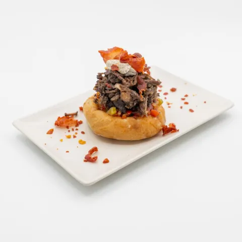 Salaílla sobre base de salsa criolla, costillas de yernera guisadas al vino tinto, con pimientos asados, mayonesa de aceitunas negras y crujiente de jamón serrano.
