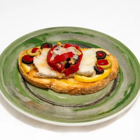 Bacalao marinado en lima con aceitunas, piquillo y cebolla perla sobre pan de carraca