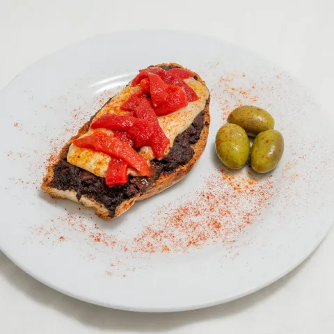 Base de pan con morcilla, queso picante, pimiento de piquillo y lluvia de pimentón