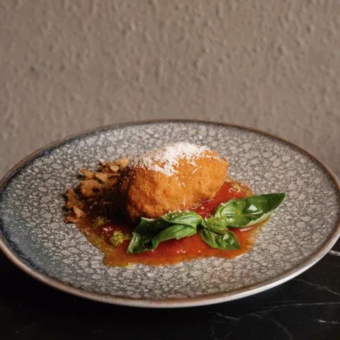 Supplì artesanal d'arròs amb tomàquet i mozzarella, servit amb parmesà, tomàquet fresc i oli d'alfàbrega