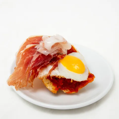 Base de pan con sobrasada casera murciana caliente, huevo de codorniz a la plancha, coronado por jamón y tocino ibérico finamente cortado