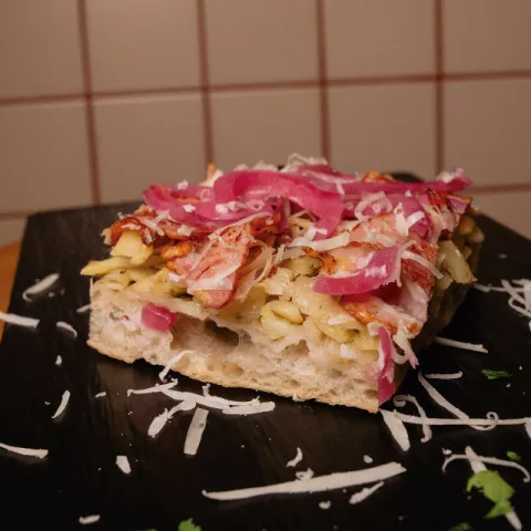 Pizza de base blanca con patata rallada y romero, beicon, cebolla encurtida y queso Mahón rallado