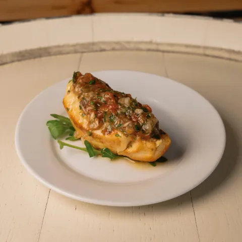 Pan de llonguet tostado cubierto de suquet tradicional de pescado, elaborado con tomàtiga de ramallet al horno, perejil, cebolla dulce y aceite de oliva