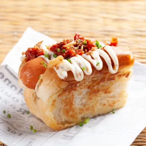 Frankfurt con tomate seco, cebolla crujiente y mayonesa de miel y mostaza en rollo de bollo.