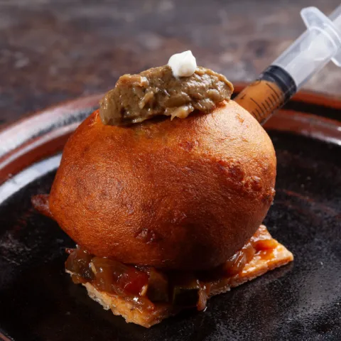 Buñuelo relleno de fricandó, con duxelles de setas y crema de queso de la Garrotxa, sobre una teja crujiente con pisto.