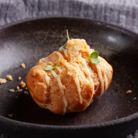 Profiterol relleno de patata y cebolla con cobertura de mayonesa y crujiente de parmesano.
