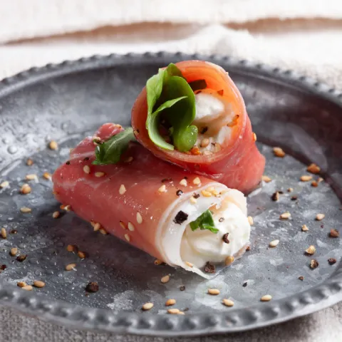 Rollito de queso fresco con jamón serrano y rúcula, aliñado con aceite y sésamo.
