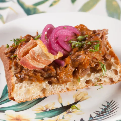 Tostada crujiente con avellanas, carne deshilachada, cebolla encurtida y crumble de avellana y panceta.
