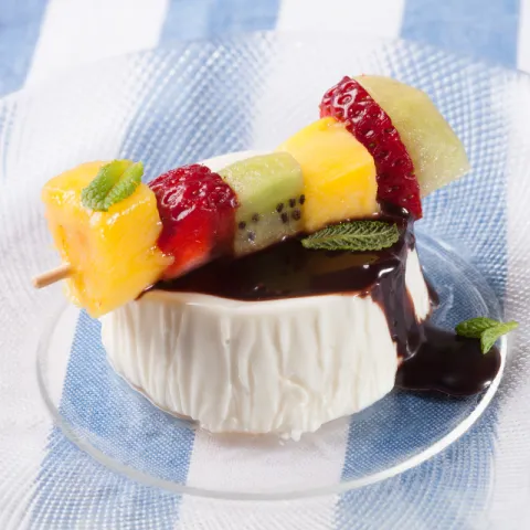 Brocheta de fruta sobre una pannacotta con chocolate.