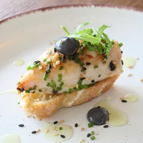 Calamar relleno de jamón serrano sobre pan tostado acompañado de rúcula, un toque de ajo y perejil y mayonesa suave con tinta de calamar