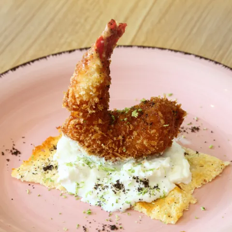 Gamba roja crujiente rebozada con panko, crema de burrata con lima y una base de crujiente de parmesano, miel y polvo de aceituna 