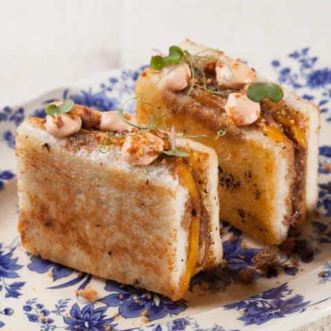 Bikini de pulled pork con cebolla caramelizada, queso cheddar y polvo de morro crujiente.