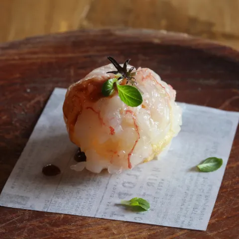 Esfera de rillette de pollo de corral y gamba roja, envuelta en una fina capa de carpaccio de gamba y salseada con la reducción del guiso y emulsión del coral