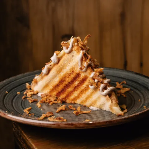 Sandwich tostado con mantequilla, relleno de jamón serrano y queso con un toque de trufa y toppings de mayonesa trufada y cebolla crujiente