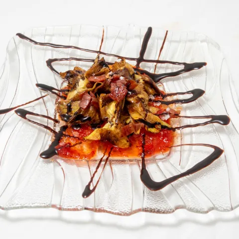 Alcachofa frita semi rebozada al punto de cocción y fritura, con viruta de jamón serrano y una base de mermelada de pimiento