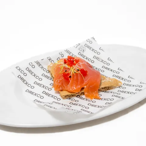 Tosta de pan crujiente cubierta con una ensaladilla de marisco y lámina de salmón ahumado con huevas rojas