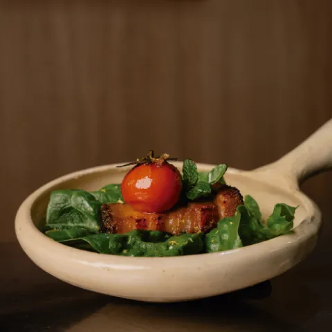 Saam de panceta marinada cocida a baja temperatura servida sobre una hoja de cogollo, menta fresca, mirin y tomate cherry confitado