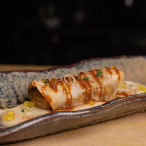 Canelón de pasta brick relleno de asado meloso de cerdo adobado acompañado de Parmentier ahumado, trufa, polvo crujiente de jamón y aceite aromatizado