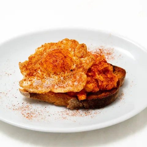 Pan tostado, sabroso revuelto de tomate frito casero, coronado con huevo de codorniz
