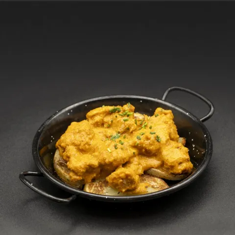 Tradicional receta de ajillo almeriense guisada con cerveza y lagarto de cerdo y servida sobre una cama de patatas paja a modo de timbal