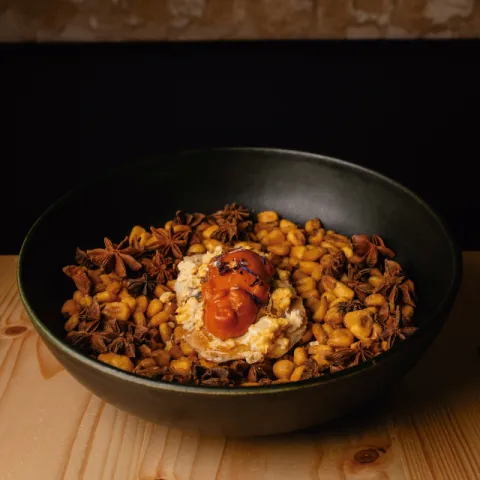 Tapa de cerdito mallorquín, sobrasada, paté, cremoso de albaricoque, miel y polvo de aceite de oliva sobre un lecho de maíz tostado
